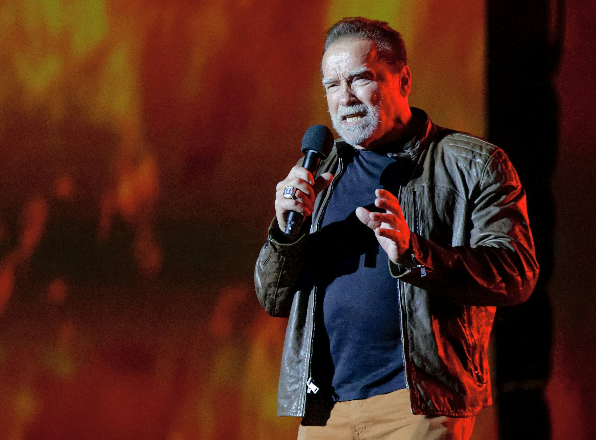 Arnold Schwarzenegger spricht in ein Mikrofon. Er trägt eine Lederjacke.