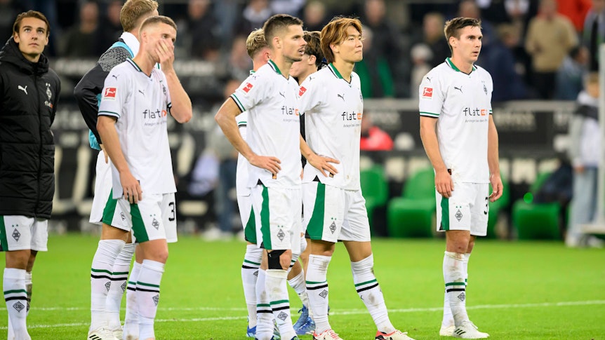 Die Gladbach-Spieler stehen auf dem Rasen und schauen enttäuscht. Im Hintergrund ist die Trainerbank.