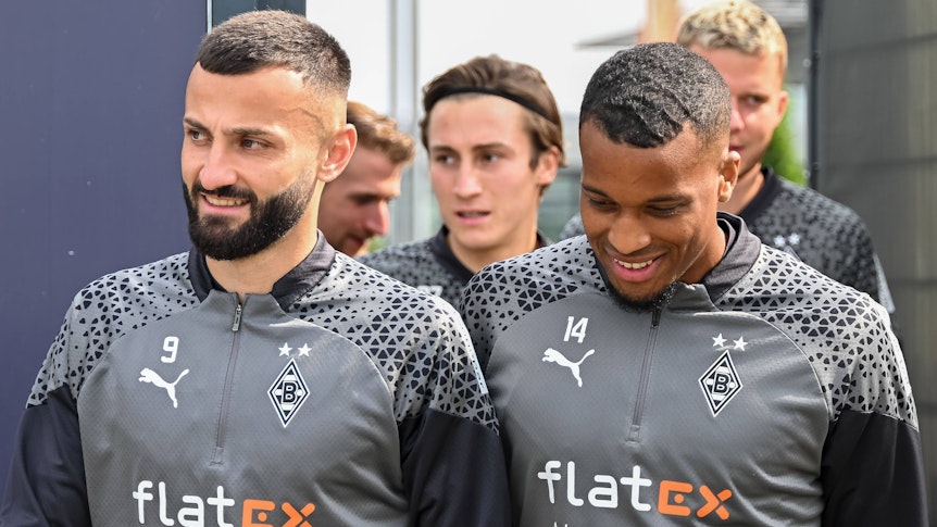 Die Spieler Honorat und Plea gehen gemeinsam auf den Trainingsplatz. Im Hintergrund sind ihre Mitspieler.