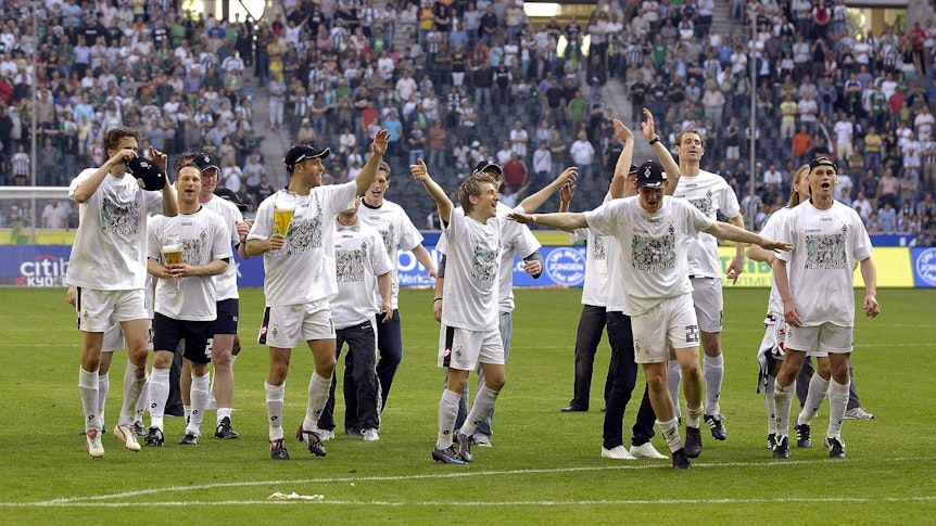 Gladbach Spieler feiern und tanzen zusammen auf dem Platz. Im Hintergrund sind die Fans.