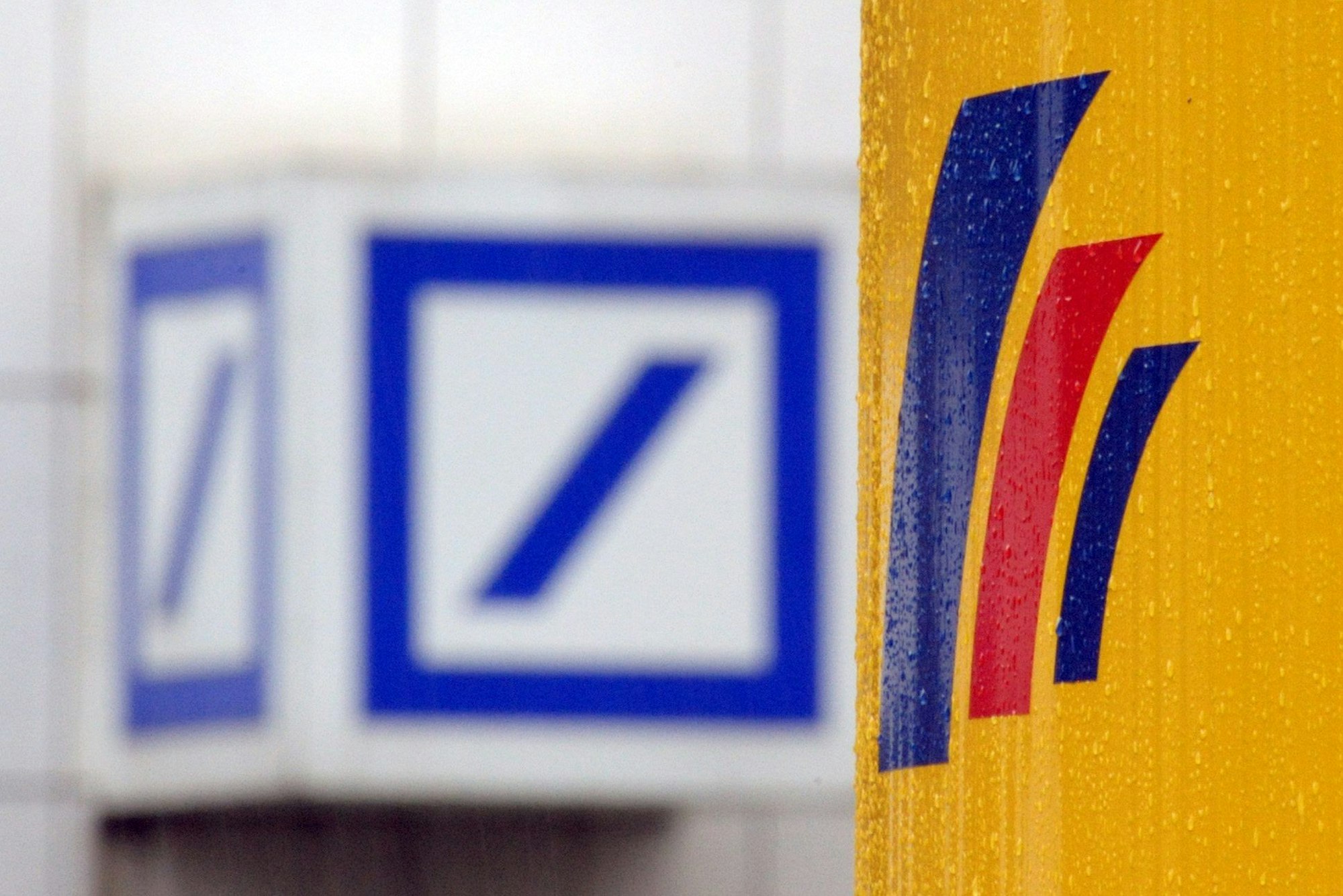 Das Logo einer Filiale der Deutschen Bank (l) und das Logo der auf der gegenüberliegenden Straßenseite befindlichen Postbank-Zentrale in Bonn.