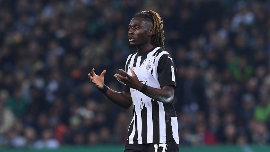 Manu Koné reißt bei einem Borussia-Spiel beide Arme vor seinen Körper.