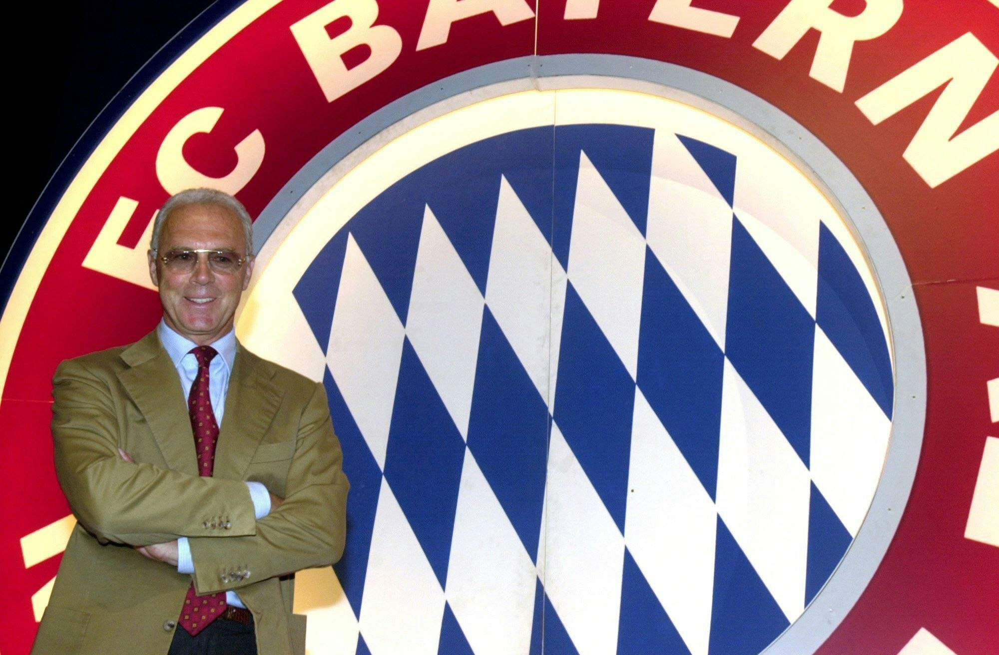 Franz Beckenbauer vor dem Logo des FC Bayern München.