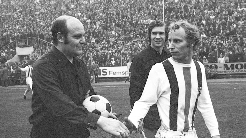 Spieler von Borussia Mönchengladbach gibt Schiedsrichter die Hand.