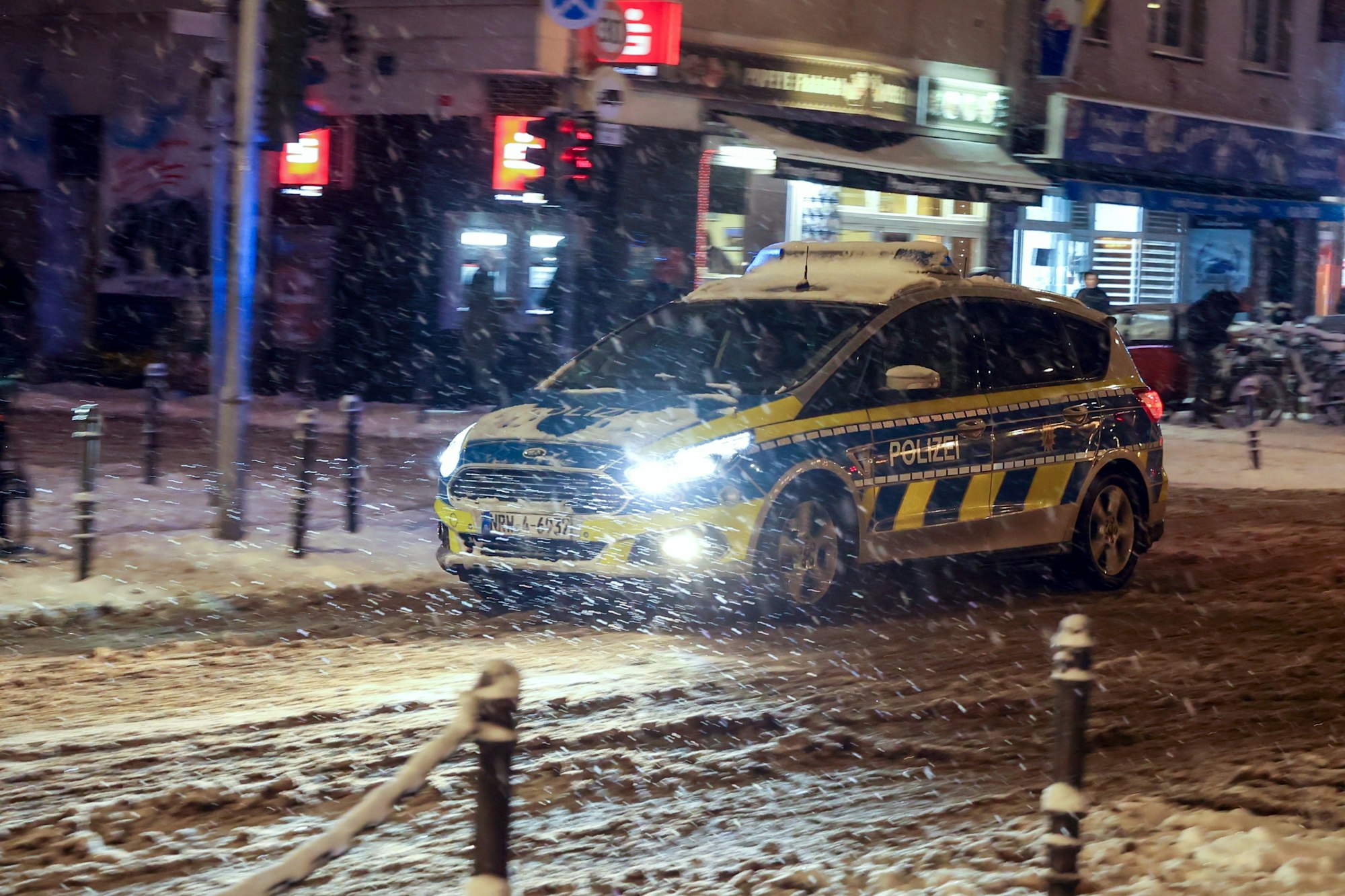 Ein Polizeiwagen fährt abends auf der Venloer Str. bei  Schneetreiben.