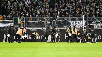 Ordner heben während eines Spiels von Borussia Mönchengladbach Schoko-Taler vom Rasen.