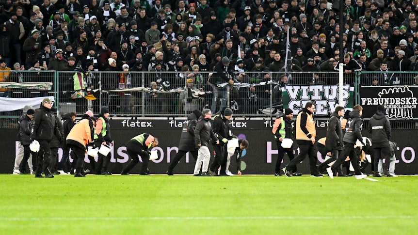 Ordner heben während eines Spiels von Borussia Mönchengladbach Schoko-Taler vom Rasen.
