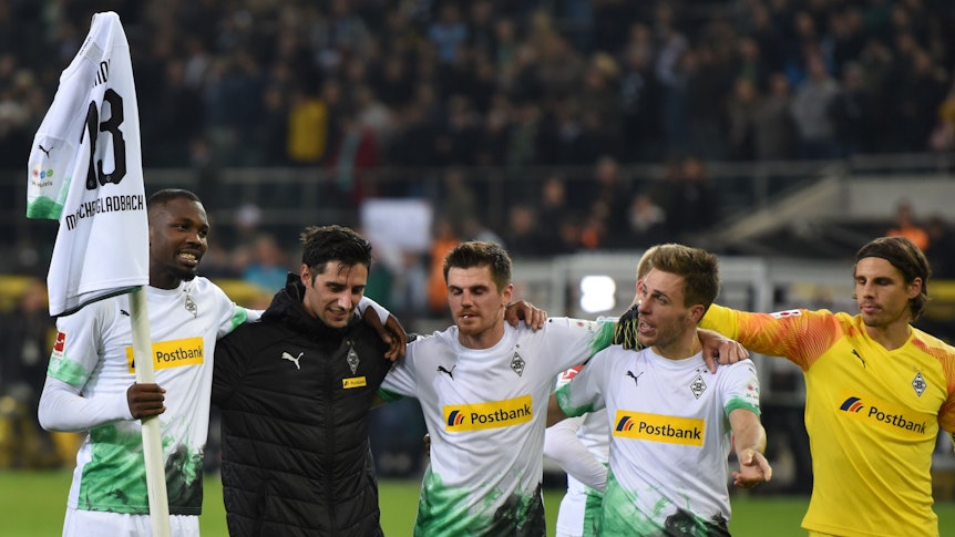 Marcus Thuram hält ein Trikot von Lars Stindl auf einer Eckfahne, Teamkollegen schauen ihm zu.