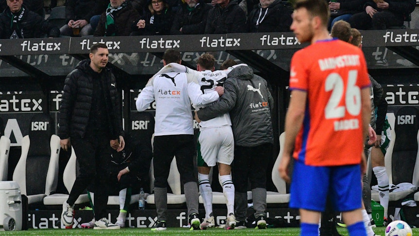 Ein Spieler von Borussia Mönchengladbach wird mithilfe von zwei Medizinern nach einer Verletzung vom Platz geführt.