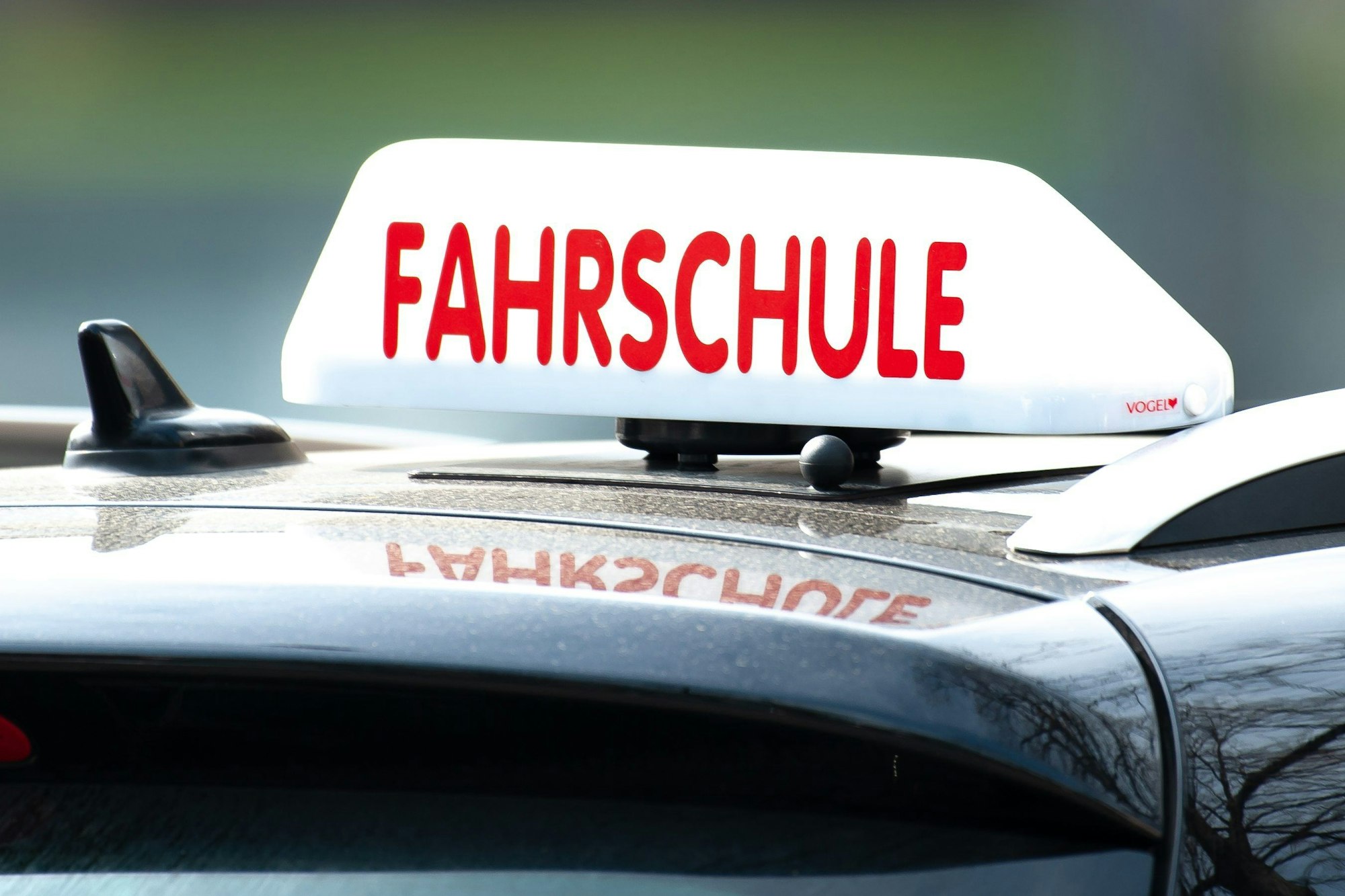 Das Foto zeigt ein Schild mit der Aufschrift „Fahrschule“ auf einem Fahrschulauto.
