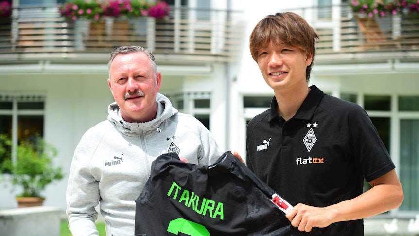 Roland Virkus und Ko Itakura halten ein Trikot des Japaners hoch.