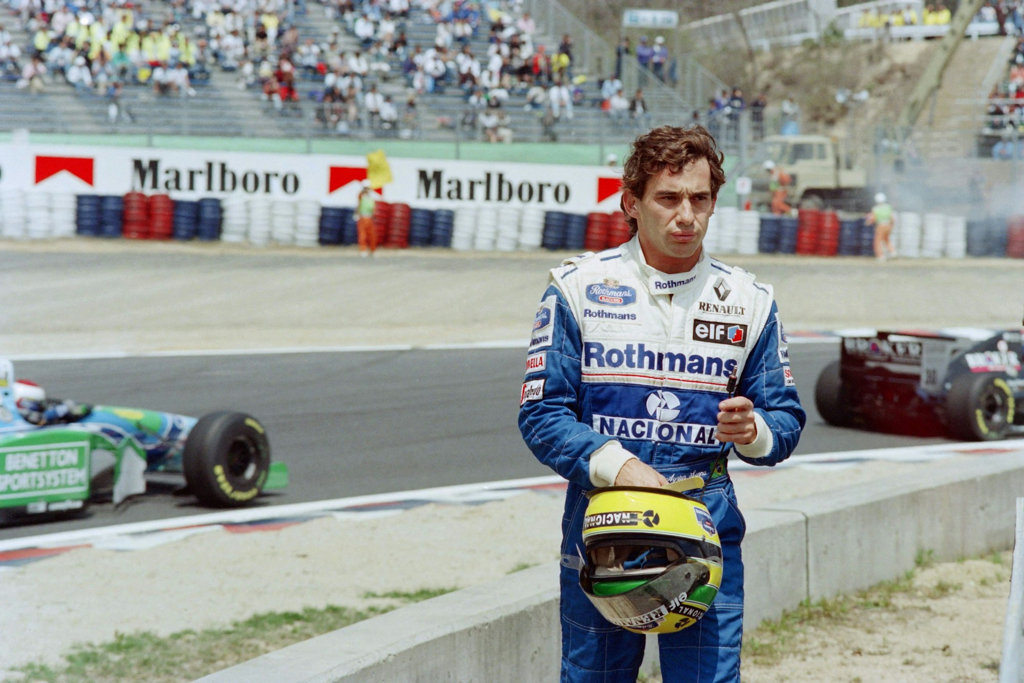 Ayrton Senna steht nach seinem Ausscheiden aus dem Pacific Grand Prix der Formel 1 der Rennstrecke, im Hintergrund fahren die anderen Autos.
