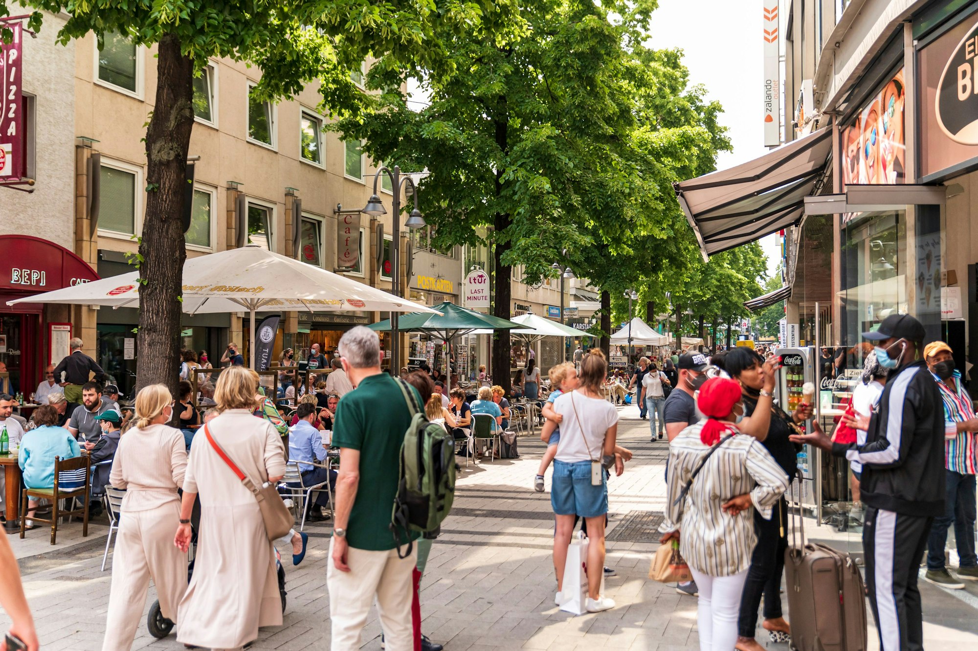 Menschen sitzen in Restaurants oder gehen durch die Breite Straße in Köln.
