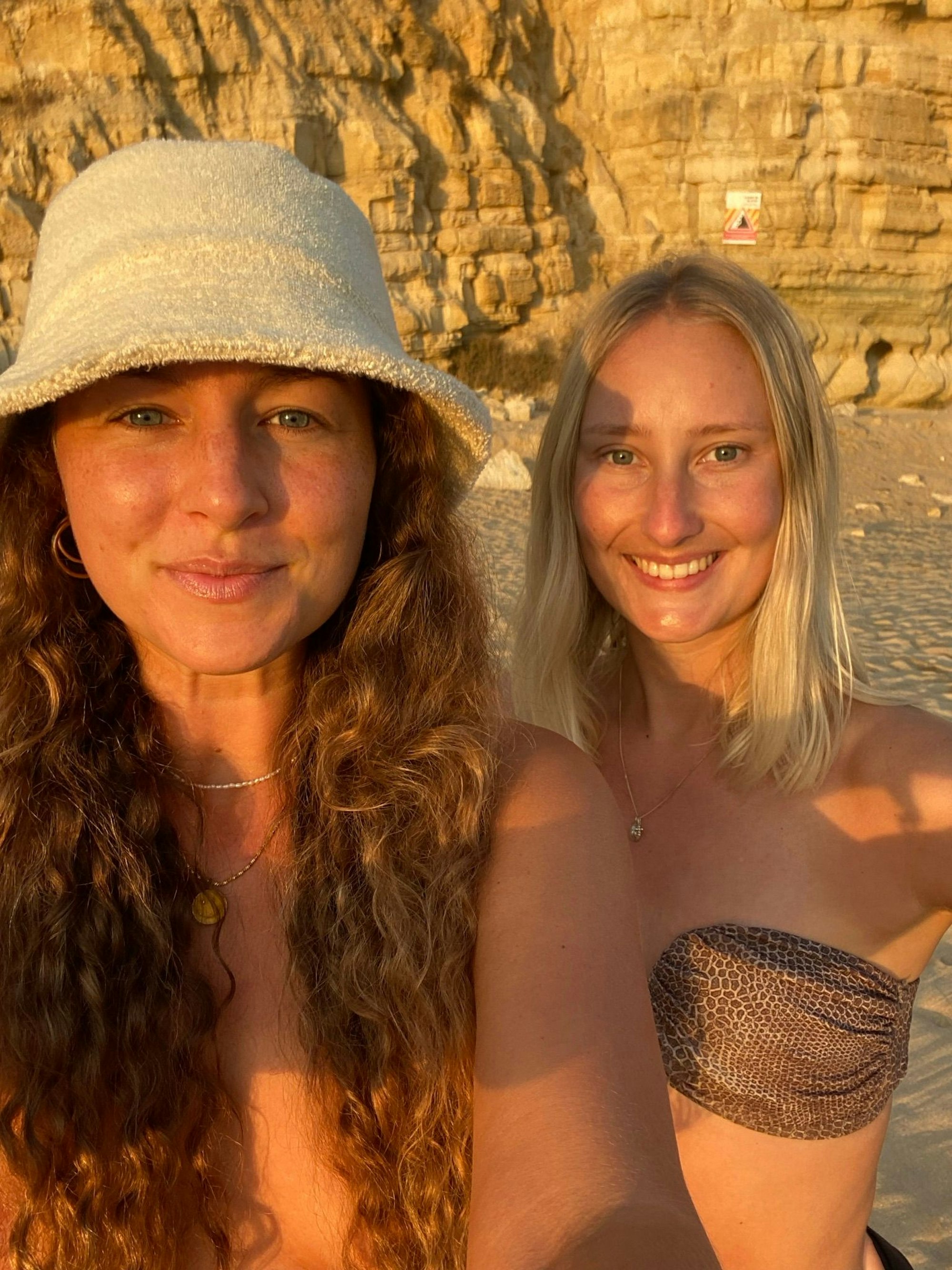 Zwei Frauen machen an einem Strand ein Selfie und grinsen in die Kamera.