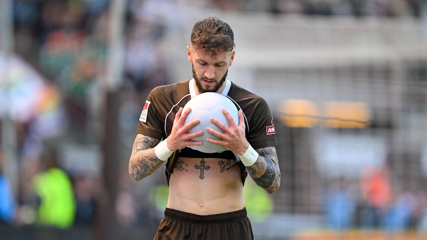 Marcel Hartel hält einen Ball mit beiden Händen fest.