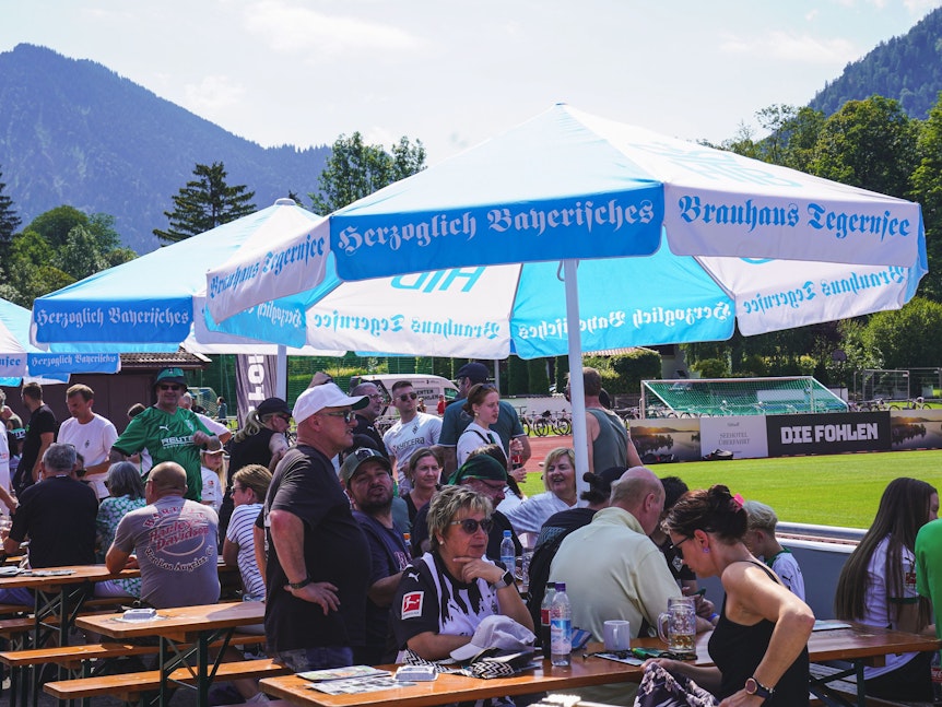 Fans von Borussia Mönchengladbach sitzen neben dem Platz an Biertischen.