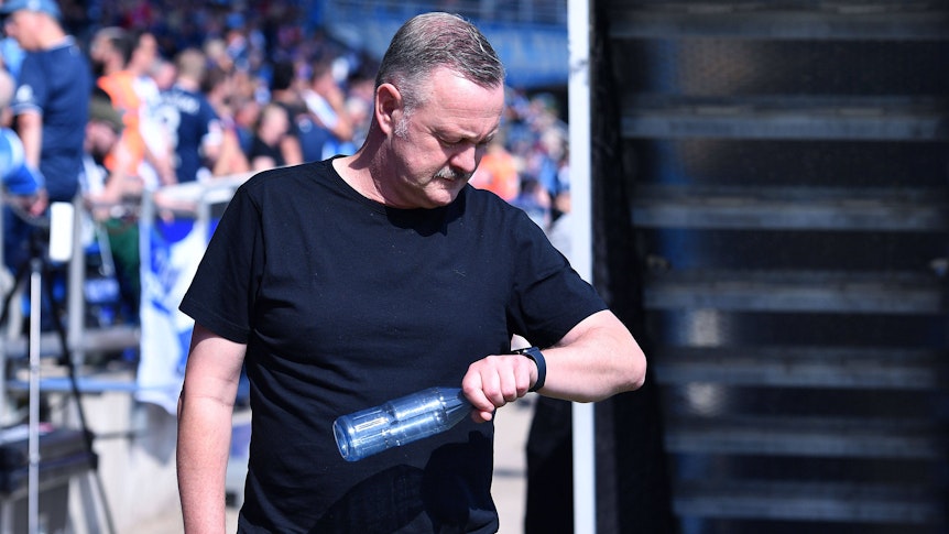 Roland Virkus schaut auf seine Armbanduhr und hält eine Wasserflasche in der Hand.