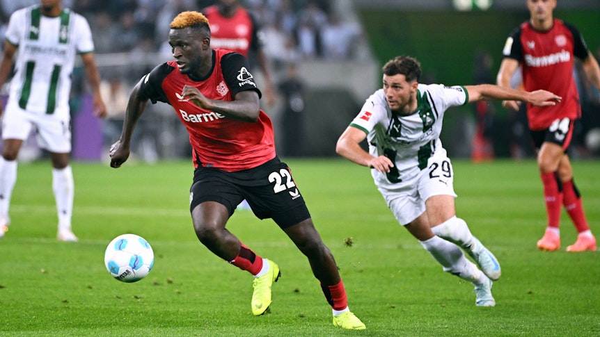 Bayer Leverkusens Victor Boniface führt den Ball, Borussia Mönchengladbachs Joe Scally verfolgt ihn.