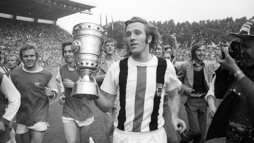 Borussia Mönchengladbachs Siegtorschütze Günter Netzer läuft mit dem DFB-Pokal in der Hand über den Platz.
