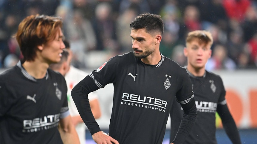 Die Gladbach-Profis Ko Itakura, Tim Kleindienst und Luca Netz stehen nach dem Spiel in Augsburg enttäuscht auf dem Rasen.