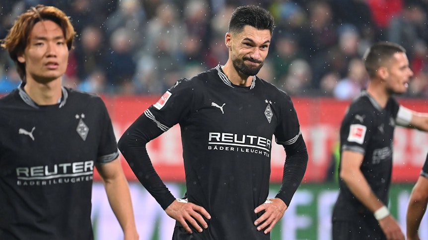 Borussia Mönchengladbachs Stürmer Tim Kleindienst steht nach dem Spiel beim FC Augsburg auf dem Rasen, hat die Arme in die Hüften gestemmt und verzieht das Gesicht.