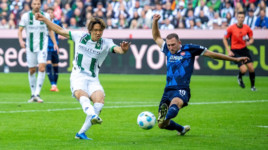 Borussia Mönchengladbachs Ko Itakura zieht ab, Heidenheims Jonas Föhrenbach versucht zu blocken.
