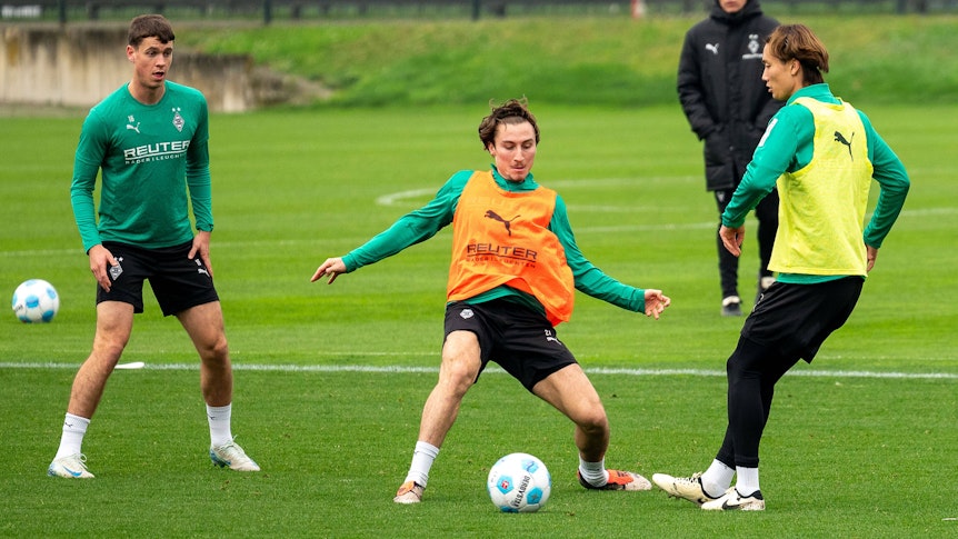 Die Gladbach-Profis Rocco Reitz und Ko Itakura kämpfen im Training um den Ball, links daneben beobachtet Philipp Sander die Szene.