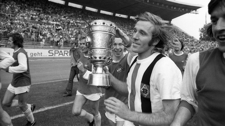 Günter Netzer hält den DFB-Pokal in den Händen auf dem Platz.