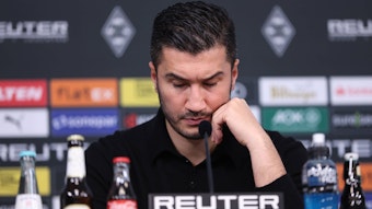 Borussia Dortmunds Trainer Nuri Sahin sitzt bei der Pressekonferenz nach dem Spiel bei Borussia Mönchengladbach auf dem Podium und stützt den Kopf auf seine linke Hand.