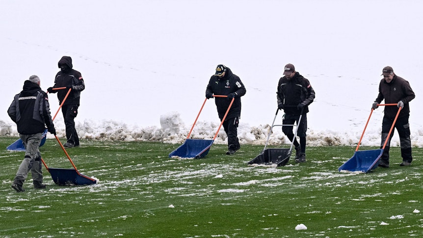 Helfer räumen mit Schneeschiebern den Schnee vom Trainingsplatz von Borussia Mönchengladbach.