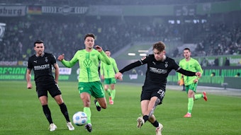 Borussia Mönchengladbachs Luca Netz schließt ab, Wolfsburgs Kilian Fischer kommt zu spät. Gladbachs Kevin Stöger beobachtet die Szene im Hintergrund.