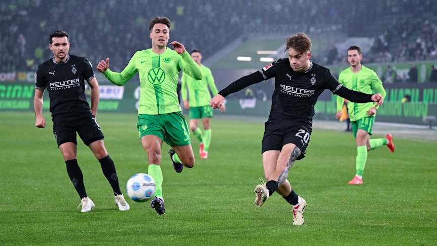 Borussia Mönchengladbachs Luca Netz schließt ab, Wolfsburgs Kilian Fischer kommt zu spät. Gladbachs Kevin Stöger beobachtet die Szene im Hintergrund.