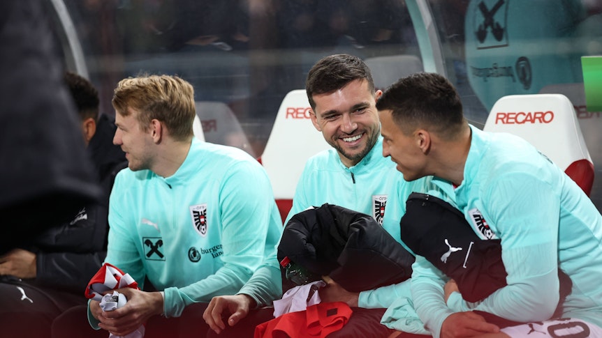 Stefan Lainer und Kevin Stöger sitzen auf der Bank und lachen miteinander.