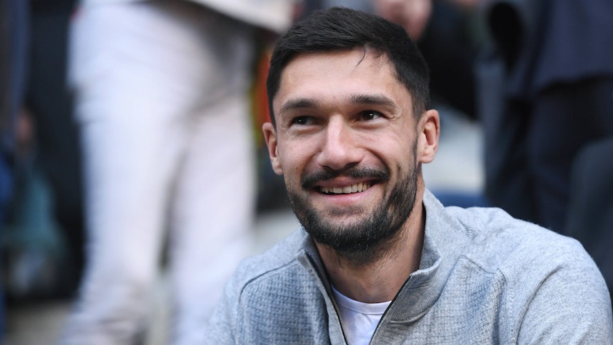 Tim Kleindienst lächelt in privater Kleidung auf der Tribüne.