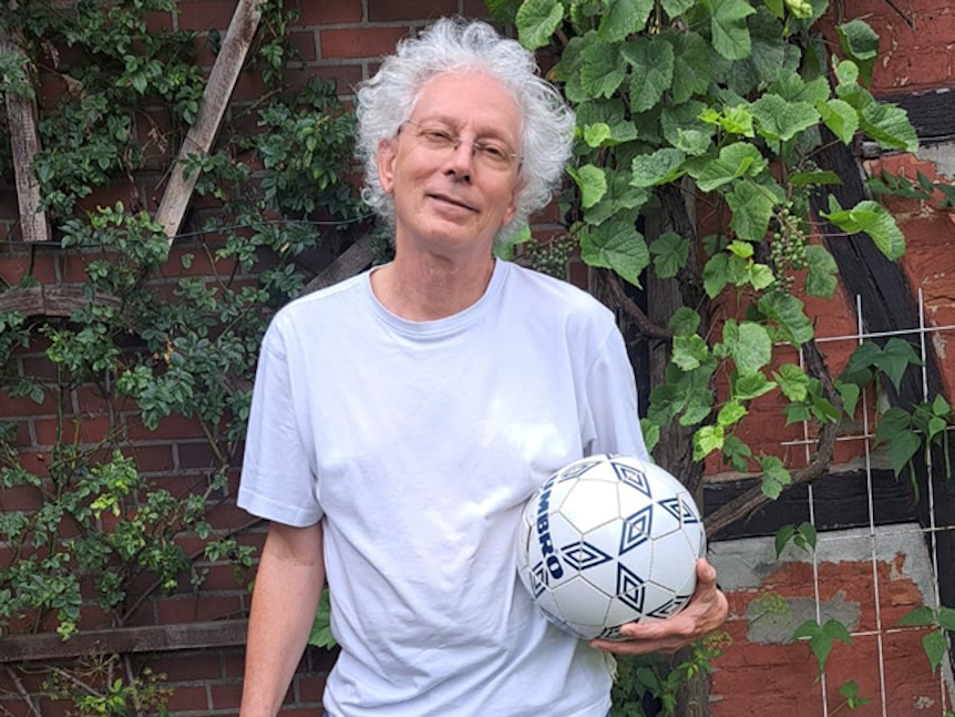 Holger Jenrich steht mit einem Ball in der Hand vor einer Hauswand.