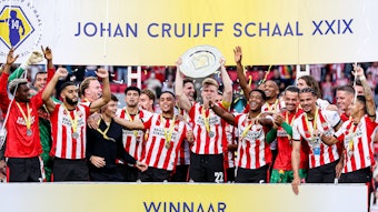Die Spieler von PSV Eindhoven jubeln mit einer Schale auf einer Tribüne.