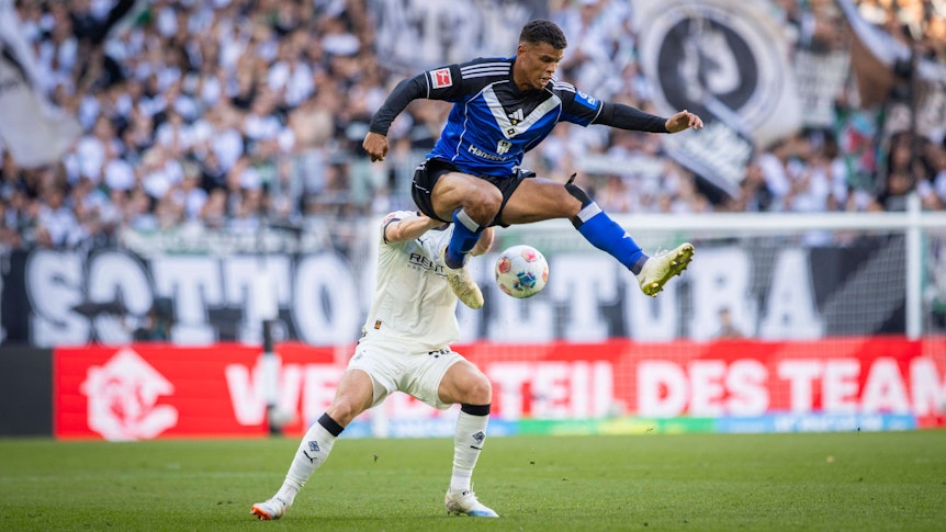 Ein Gladbach-Spieler schubst einen HSV-Profi in der Luft.