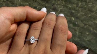 Eine Frauen-Hand mit einem Verlobungsring am Finger vor dem Meer.