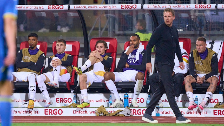 Rocco Reitz und mehrere Nationalspieler sitzen hinter Bundestrainer Julian Nagelsmann auf der Bank.