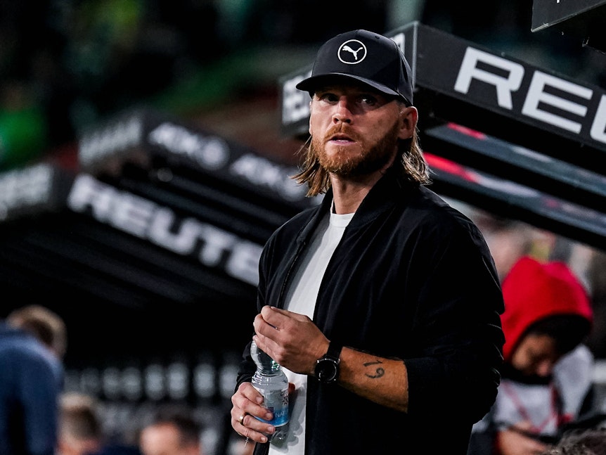 Trainer Eugen Polanski steht an der Seitenlinie mit einer Flasche in der Hand.