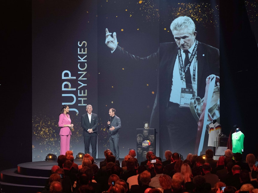 Ein Bild von Jupp Heynckes mit dem Champions-League-Pokal wird auf einer großen Leinwand gezeigt.