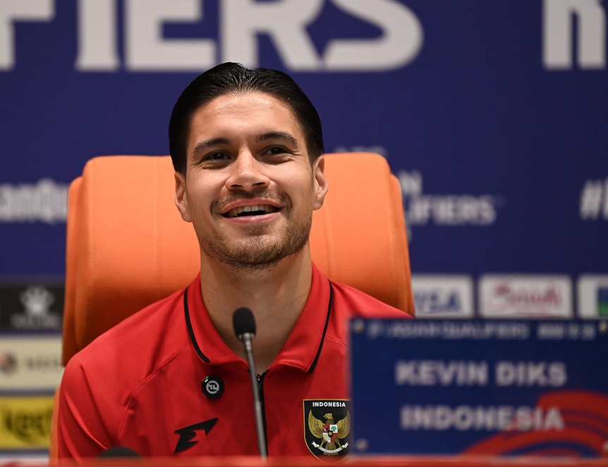 Lächelnder Kevin Diks in rotem Trikot mit indonesischem Wappen bei Pressekonferenz.