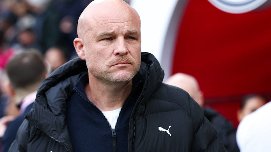 Glatzköpfiger Mann mit Bart, schwarzer Jacke, Puma-Logo und Salzburg-Schriftzug schaut ernst