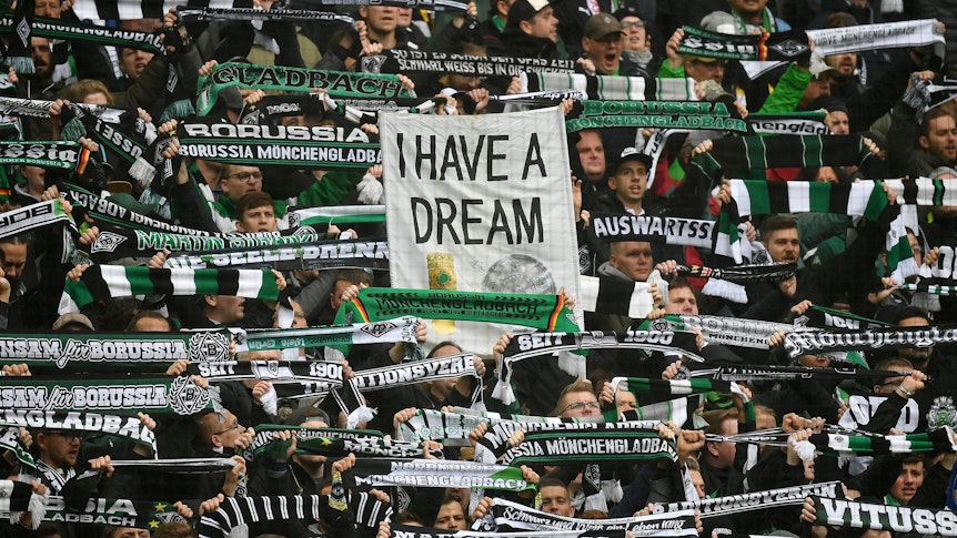 Gladbach-Fans zeigen ein Plakat mit der Aufschrift „I HAVE A DREAM“ und dem Bild von Meisterschale und DFB-Pokal.