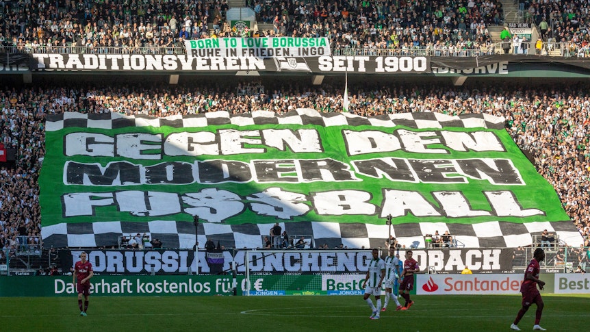Gladbacher Fußballfans in der Nordkurve halten ein Banner mit der Aufschrift „Gegen den Modernen Fussball“ hoch.