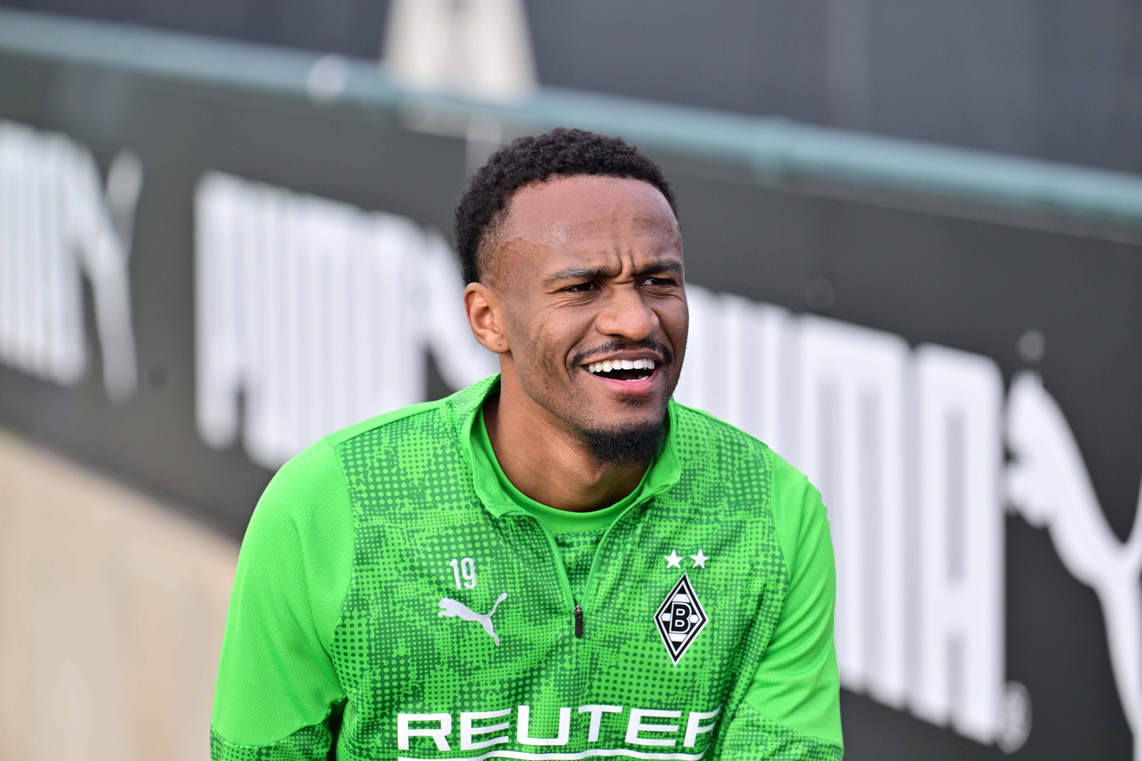 Nathan Ngoumou lächelt in Gladbachs Trainingsklamotten.